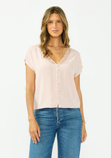 [Color: Shell] A front facing image of a brunette model wearing a pink lace trim top with short dolman sleeves and a button front. 