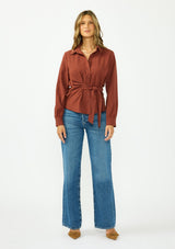 [Color: Terracotta] A front facing image of a brunette model wearing a rust button down shirt with a tie waist, collared neck, and long sleeves with button cuffs. 