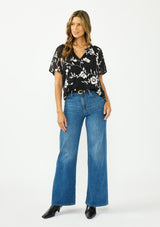 [Color: Black] A front facing image of a brunette model wearing a white and black embroidered chiffon top with short sleeves and a v neckline. 
