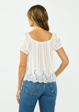 [Color: White] A back facing image of a brunette model wearing a sheer white satin top with stripes, a lace trim hem, puff sleeves, and a drawstring neckline. 