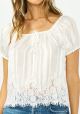 [Color: White] A detail image of a brunette model wearing a sheer white satin top with stripes, a lace trim hem, puff sleeves, and a drawstring neckline. 
