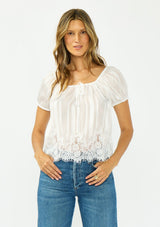 [Color: White] A front facing image of a brunette model wearing a sheer white satin top with stripes, a lace trim hem, puff sleeves, and a drawstring neckline. 