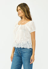 [Color: White] A side facing image of a brunette model wearing a sheer white satin top with stripes, a lace trim hem, puff sleeves, and a drawstring neckline. 