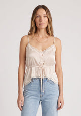 [Color: Antique Blush] A front facing image of a blonde model wearing a light pink poly satin lace trim top with  a button front, adjustable spaghetti straps, and a drawstring waist with tie detail. Paired with a classic light wash denim. 