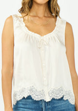 [Color: Ivory] A detail image of a brunette model wearing an ivory poly satin tank top with a ruffled v neckline, tie front, button front, and a lace trim hem. 