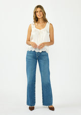 [Color: Ivory] A front facing image of a brunette model wearing an ivory poly satin tank top with a ruffled v neckline, tie front, button front, and a lace trim hem. 