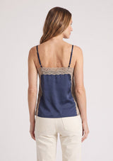 [Color: Navy/Taupe] A back facing image of a blonde model wearing a navy satin camisole with lace trim, adjustable spaghetti straps, and side slits. 