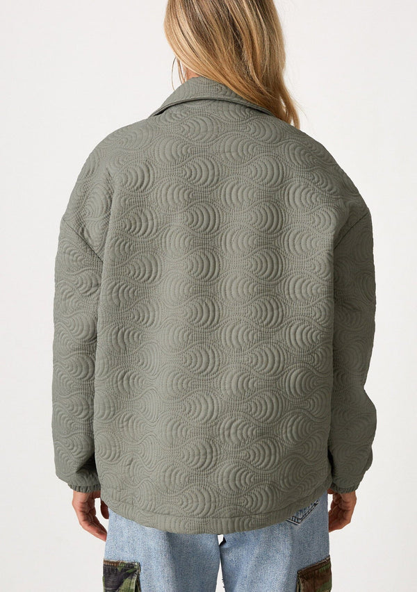 [Color: Olive] A back facing image of a blonde model wearing an olive green quilted jacket. With a zip front, long sleeves, a drawstring waist with adjustable toggles, and a funnel neck.
