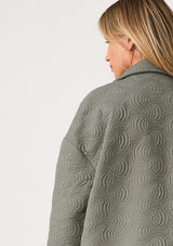 [Color: Olive] A close up back facing image of a blonde model wearing an olive green quilted jacket. With a zip front, long sleeves, a drawstring waist with adjustable toggles, and a funnel neck.
