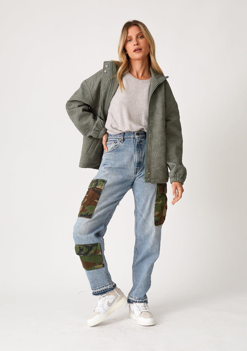 [Color: Olive] A full body front facing image of a blonde model wearing an olive green quilted jacket. With a zip front, long sleeves, a drawstring waist with adjustable toggles, and a funnel neck.