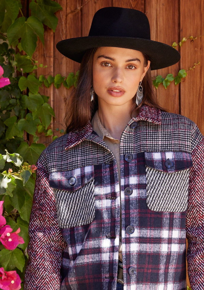 [Color: Wine/Navy] A close up front facing image of a brunette model standing outside wearing a classic shirt jacket in a wine red and navy blue patchwork plaid. A soft fall and winter jacket with long sleeves, front patch flap pockets, a collared neckline, a button up front, and side pockets.
