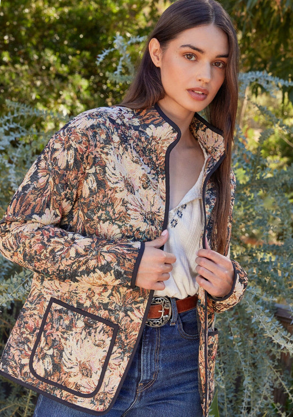 [Color: Black/Natural] A front facing image of a brunette model wearing a bohemian jacket in a black and natural floral tapestry. With long sleeves, a dropped shoulder, an open front, and side patch pockets. 