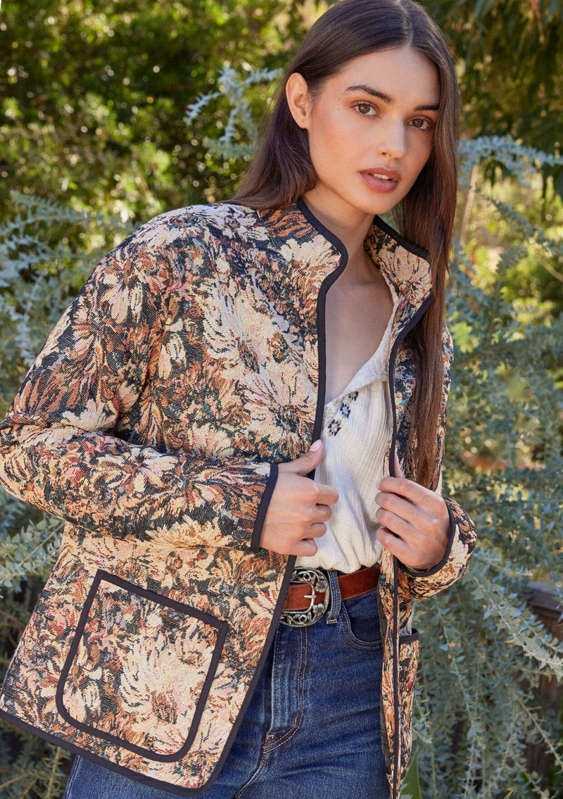 [Color: Black/Natural] A front facing image of a brunette model wearing a bohemian jacket in a black and natural floral tapestry. With long sleeves, a dropped shoulder, an open front, and side patch pockets. 