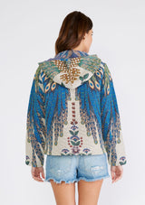 [Color: Natural/Teal] A half body back facing image of a brunette model wearing a bohemian statement hoodie in a natural and teal blue peacock tapestry design. With long sleeves, a front zip closure, side pockets, and a drawstring hoodie. 