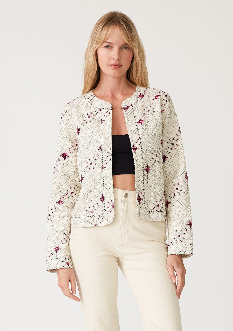 [Color: Natural/Fuchsia] A half body front facing image of a blonde model wearing a lightweight bohemian spring jacket in ivory with pink embroidered detail and contrast black thread detail. With long sleeves, an open front, and a cropped fit. 