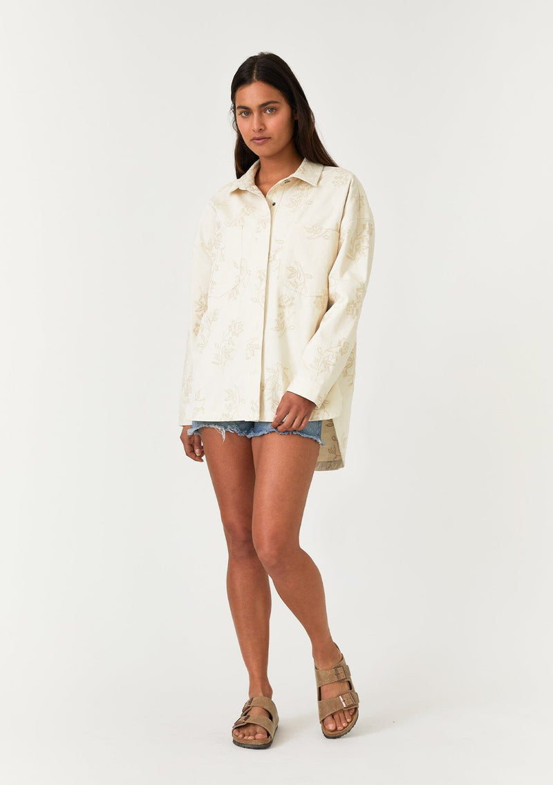 [Color: Natural] A full body front facing image of a brunette model wearing an off white bohemian shirt jacket crafted from cotton. With long sleeves, a collared neckline, a snap button front, front patch pockets, and tonal embroidered detail throughout. 