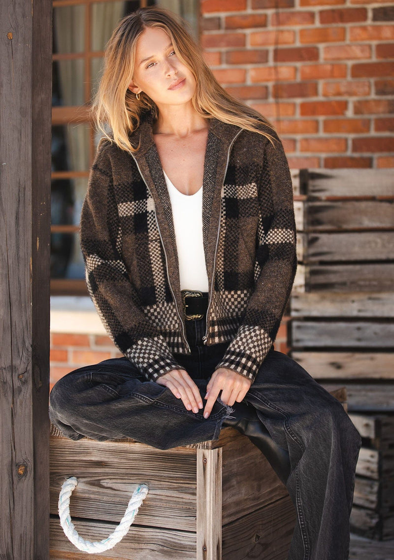 [Color: Brown/Taupe] A front facing image of a blonde model wearing a fall season black and brown plaid jacket with a zip up front and side pockets. 