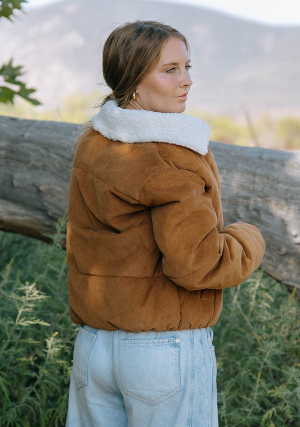 [Color: Camel] A back facing image of a brunette model wearing a brown corduroy puffer jacket with a sherpa collar, zip-up front, and welt pockets. 