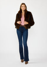 Woman wearing a brown fur coat, pink shirt, and blue jeans on a white background