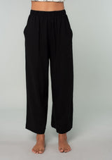 [Color: Black] A front facing image of a brunette model wearing a cool black linen and cotton blend lounge pant. With side pockets, an elastic waistband, and a wide leg. 