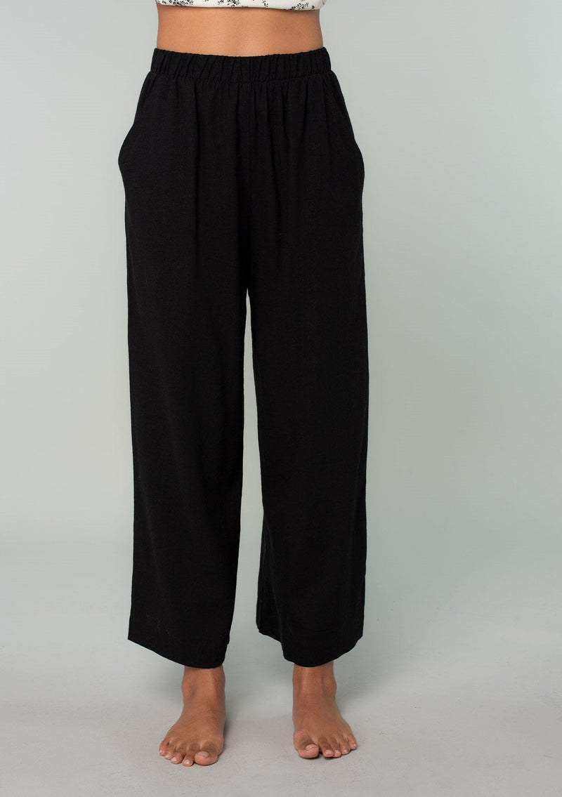 [Color: Black] A front facing image of a brunette model wearing a cool black linen and cotton blend lounge pant. With side pockets, an elastic waistband, and a wide leg. 
