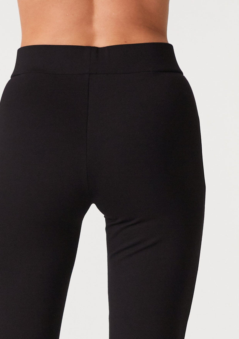 [Color: Black] A close up back facing image of a blonde model wearing a slim fit black flared legging designed in Ponte. With an elastic waist. 