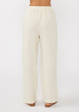 [Color: Tea Dye] A back facing image of a light beige pant crafted in cotton gauze with an elastic drawstring waistband, side pockets, and wide legs. Ideal for beach styling and lounging. 