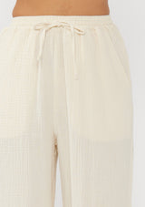 [Color: Tea Dye] A detail image of a light beige pant crafted in cotton gauze with an elastic drawstring waistband, side pockets, and wide legs. Ideal for beach styling and lounging. 