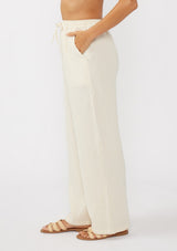 [Color: Tea Dye] A side facing image of a light beige pant crafted in cotton gauze with an elastic drawstring waistband, side pockets, and wide legs. Ideal for beach styling and lounging. 