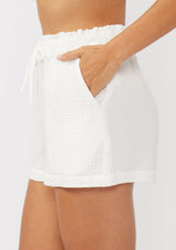 [Color: White] A side facing image of white cotton gauze shorts with an elastic drawstring waist and side pockets. Perfect for spring, lounging, or beach days. 