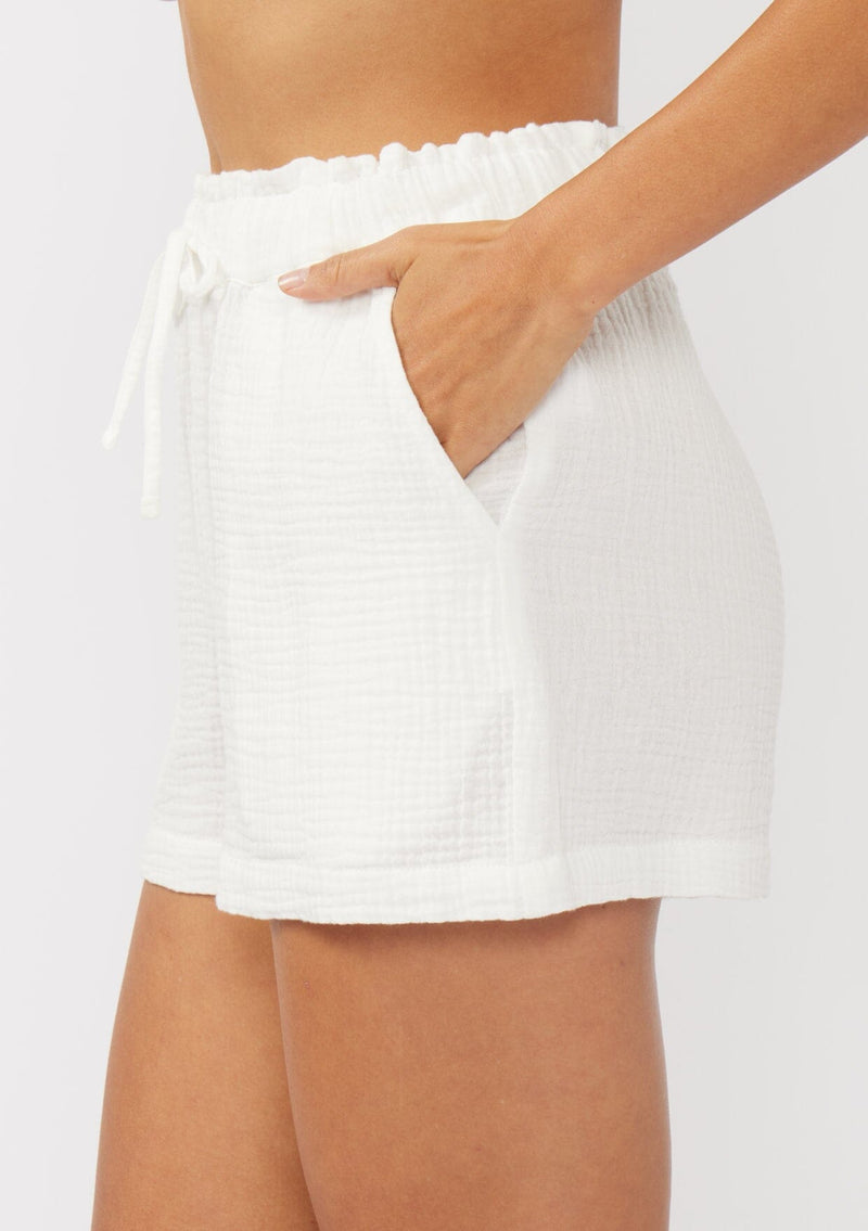 [Color: White] A side facing image of white cotton gauze shorts with an elastic drawstring waist and side pockets. Perfect for spring, lounging, or beach days. 