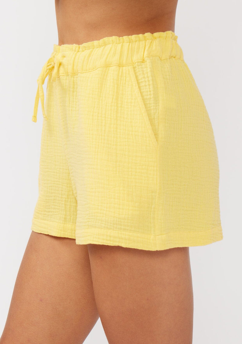 [Color: Yellow] A side facing image of yellow cotton gauze shorts with an elastic drawstring waist and side pockets. Perfect for spring, lounging, or beach days. 