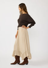 [Color: Taupe] A side facing image of a brunette model wearing a taupe maxi length skirt. With a trendy low rise waist, a ruffled hemline, smocked elastic waist details, and a flowy silhouette.