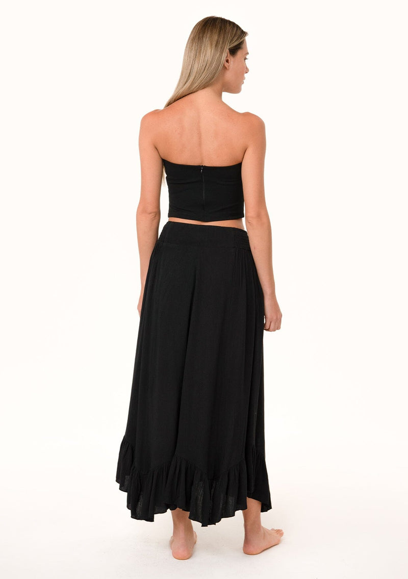 [Color: Black] A back facing image of a blonde model wearing a black maxi length skirt. With a trendy low rise waist, a ruffled hemline, smocked elastic waist details, and a flowy silhouette.