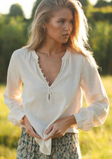 [Color: Natural] A front facing image of a blonde model wearing an off white cotton jacquard blouse with long sleeves, button cuffs, and button front. 