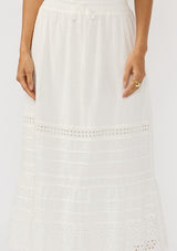 [Color: White] A detail image of brunette model wearing a white bohemian maxi skirt with an eyelet trim, pintucks, and an elastic drawstring waist.