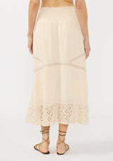 [Color: Natural] A back facing image of a beige bohemian maxi skirt with a smocked waist and lace trims. 