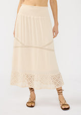 [Color: Natural] A front facing image of a beige bohemian maxi skirt with a smocked waist and lace trims. 
