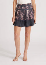 [Color: Grey/Dusty Rose] A front facing image of a grey floral pleated skirt with a satin hem, clipped lurex, paperbag waist, and side tie details. 