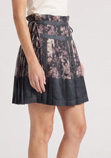 [Color: Grey/Dusty Rose] A side facing image of a grey floral pleated skirt with a satin hem, clipped lurex, paperbag waist, and side tie details. 