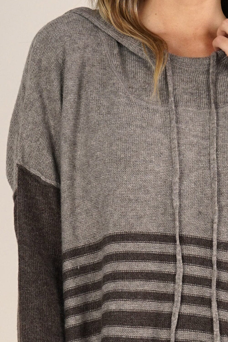 [Color: Cement/Dark Chocolate] An image of a blonde model wearing a grey and brown striped pullover hoodie with a contrast sleeve, drawstring, and kangaroo pockets. Casual and laid back for the fall season. 
