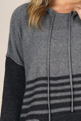 [Color: Grey/Charcoal] An image of a blonde model wearing a grey striped pullover hoodie with a contrast sleeve, drawstring, and kangaroo pockets. Casual and laid back for the fall season. 