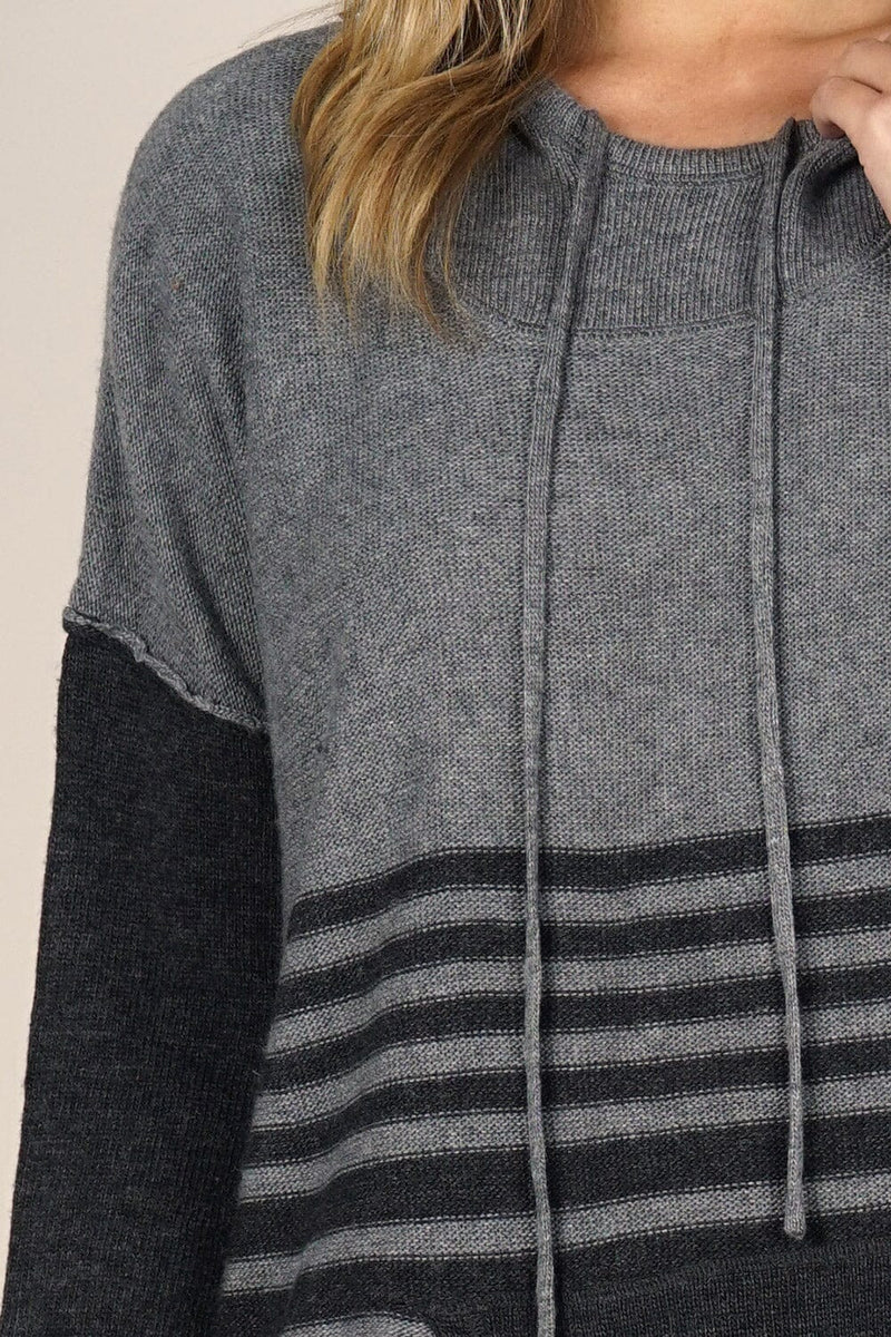[Color: Grey/Charcoal] An image of a blonde model wearing a grey striped pullover hoodie with a contrast sleeve, drawstring, and kangaroo pockets. Casual and laid back for the fall season. 