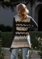 [Color: Black/Grey] A back facing image of a blonde model wearing an abstract cardigan with an adjustable waist belt. 