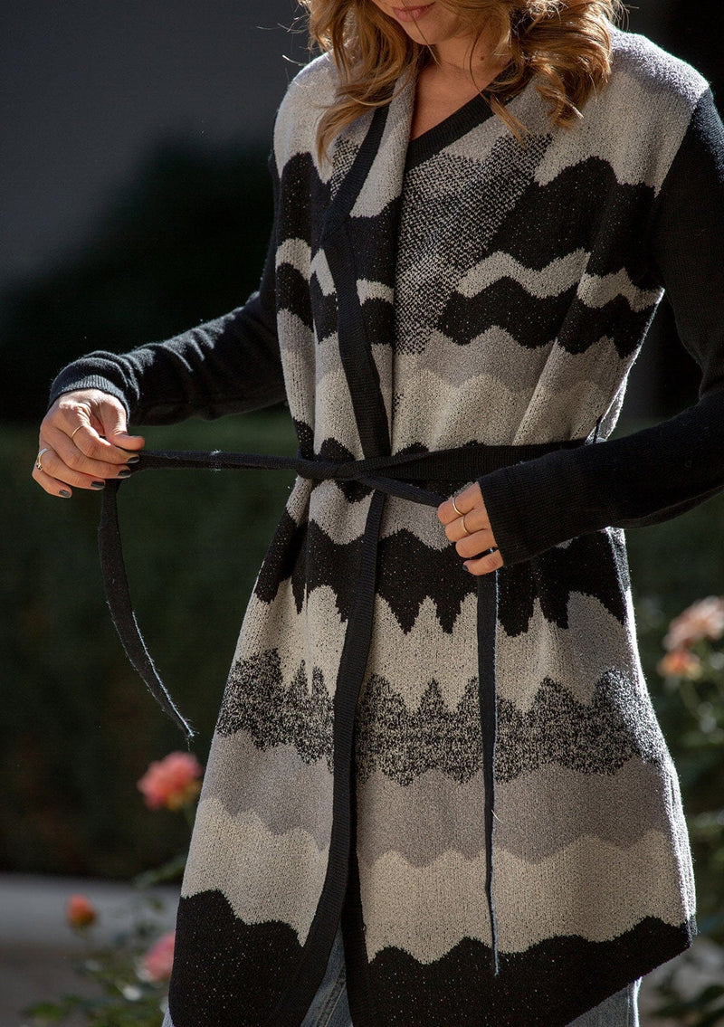 [Color: Black/Grey] A detail image of a blonde model wearing an abstract cardigan with an adjustable waist belt. 