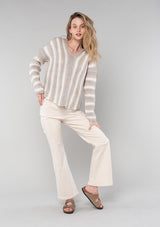[Color: Ash/Cream] A front facing image of a blonde model wearing a vertical striped knit pullover with a hoodie, relaxed v-neckline, and cozy long sleeves. A classic knit sweater for casual outings. 