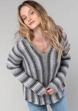 [Color: Smoke/Steel] A detail image of a blonde model wearing a vertical striped knit pullover with a hoodie, relaxed v-neckline, and cozy long sleeves. A classic knit sweater for casual outings. 