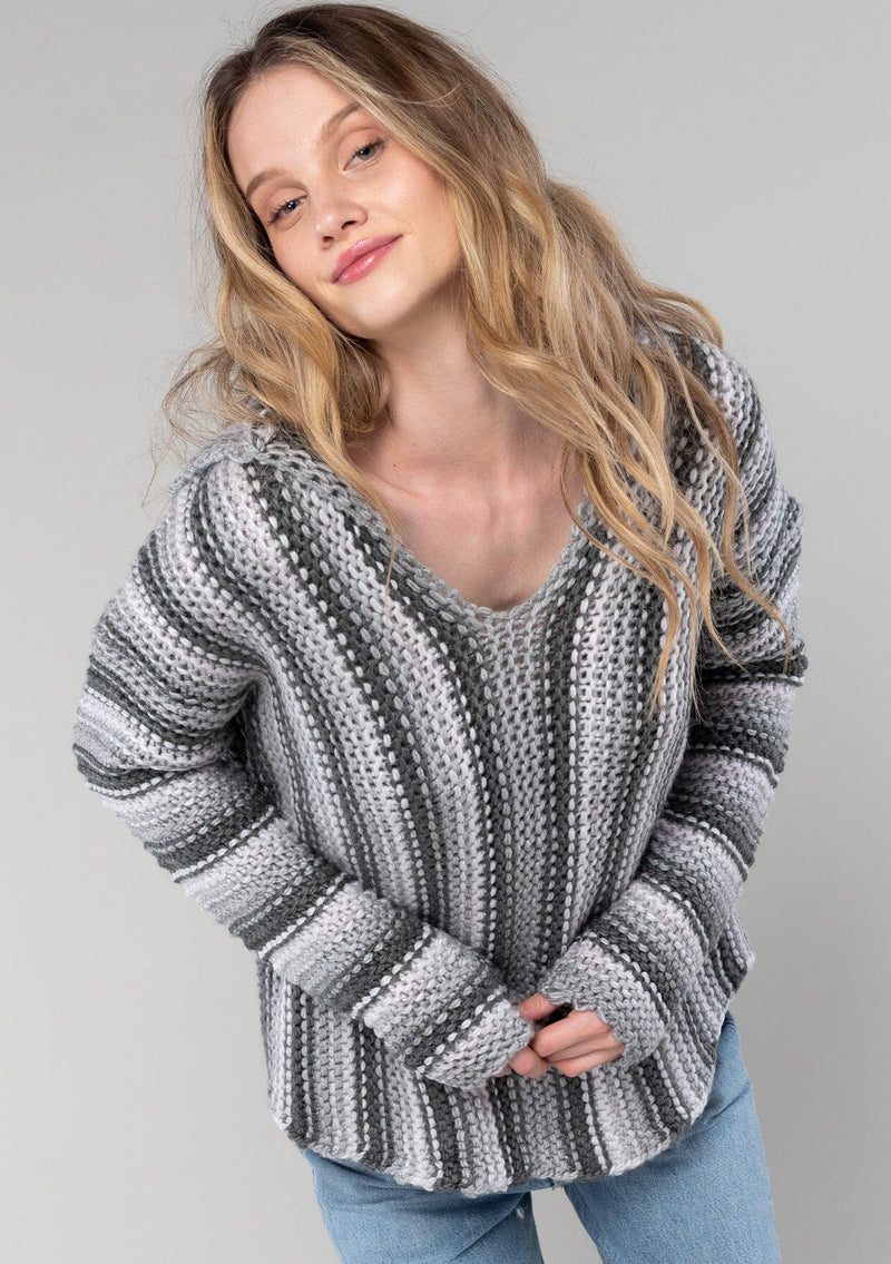 [Color: Smoke/Steel] A detail image of a blonde model wearing a vertical striped knit pullover with a hoodie, relaxed v-neckline, and cozy long sleeves. A classic knit sweater for casual outings. 