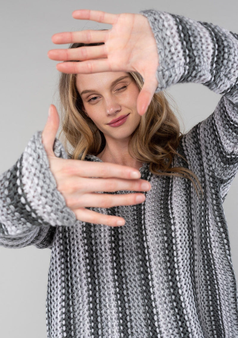 [Color: Smoke/Steel] A detail image of a blonde model wearing a vertical striped knit pullover with a hoodie, relaxed v-neckline, and cozy long sleeves. A classic knit sweater for casual outings. 