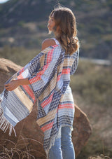 [Color: Navy/Vanilla] A side facing image of a blonde model wearing a geometric stripe knit bohemian poncho with an open front and fringe trim. 